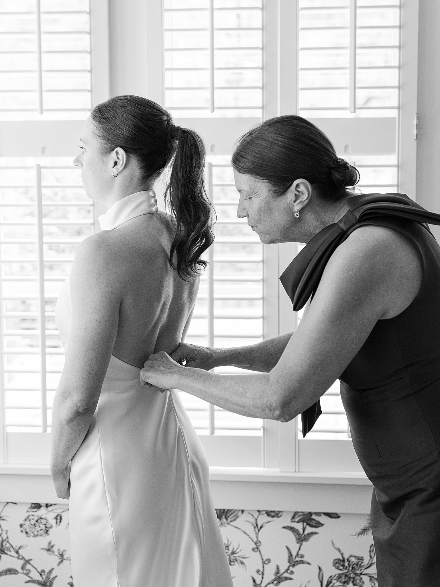 mother helping her daughter into her wedding dress in black and white